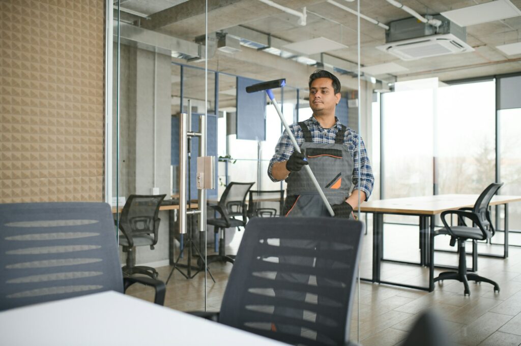 Male janitor cleaning window in office